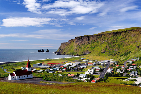 冰島南部維克小鎮(Vík í Mýrdal)
是環島公路上的重要驛站,距離雷克雅未克約 180-200 公里,人口僅約 300-600 人。這座安寧的小鎮被壯麗自然包圍,以經典的紅色屋頂教堂、神祕的雷尼斯黑沙灘(Reynisfjara)及卡特拉火山(Katla)景觀聞名。它也是重要的旅遊補給站,提供超市、加油站和住宿服務。