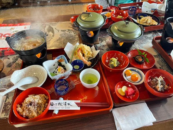 日式傳統餐館: 體驗當地的懷石料理:(含中餐)
日式餐館全名為「梅ケ枝清水」,是一間在旧城下町擁有155年歷史,由和風老房子翻新後的當地餐館。在當地相當受歡迎,是必須事先預定的特色餐館。在日本這樣的老房子被稱作「古民家」,沉靜而復古的氛圍饒富療癒之情!
店內主打使用山形縣東根名水、季節時蔬與特產製作特色料理,不僅能感受到日式家常菜的溫暖,更能品嘗到高齡89歲(2024年)的店主橫田奶奶滿滿的人情味與日式接待,為我們準備的道地和風懷石料理喔。
用餐內容: 鍋物*1 , 炸物(依季節:或為肉類,或為魚類,蝦類) , 湯類 , 果醋一杯 , 日式菇類蒸油飯一碗(可續碗1次), 渍物 ,綠茶一杯 , 季節水果